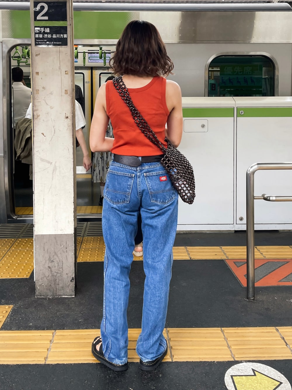 オレンジ系のタンクトップ、ブルー系のデニムパンツ、ブラック系のサンダルを着用したレディースの秋コーディネートの2枚目の写真