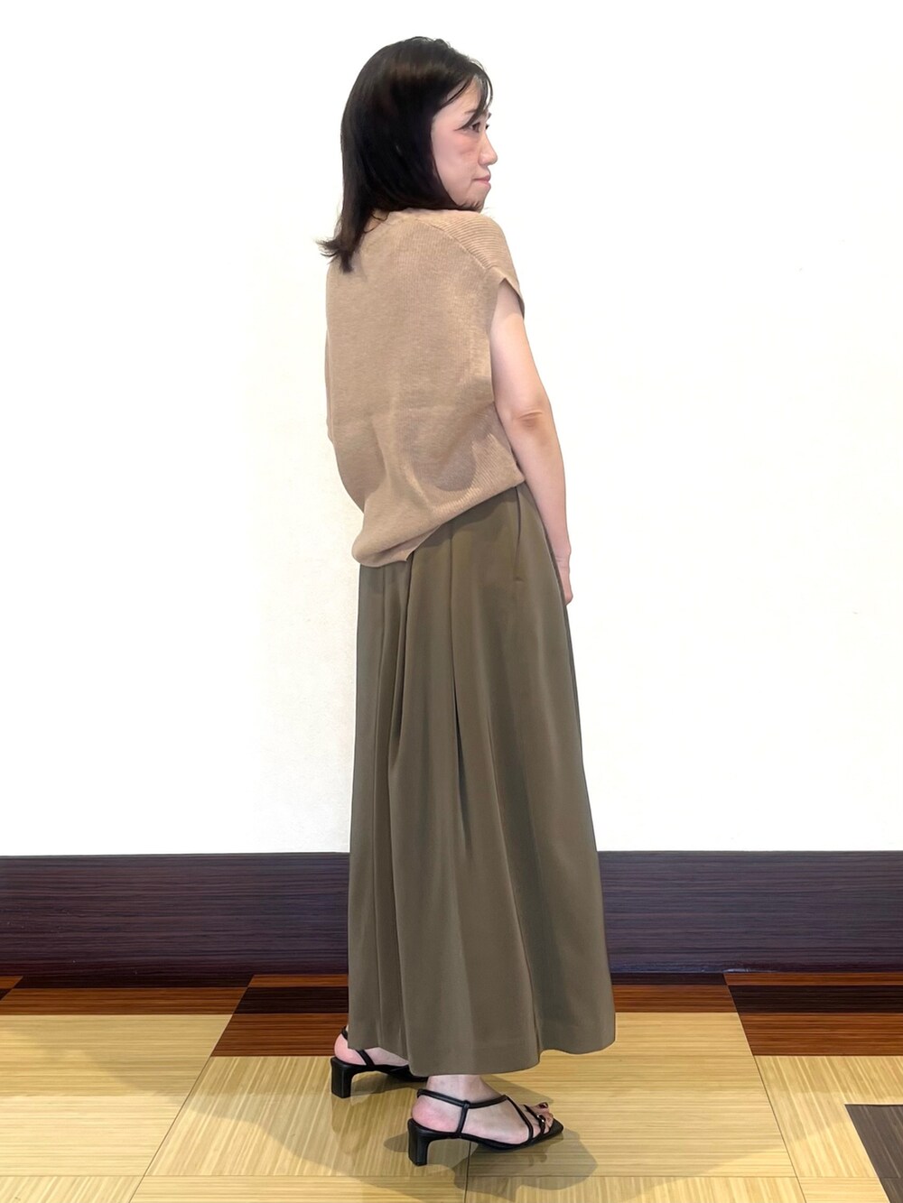 ベージュ系のカーディガン/ボレロ、グリーン系のスカート、ブラック系のサンダルを着用したレディースの秋コーディネートの2枚目の写真