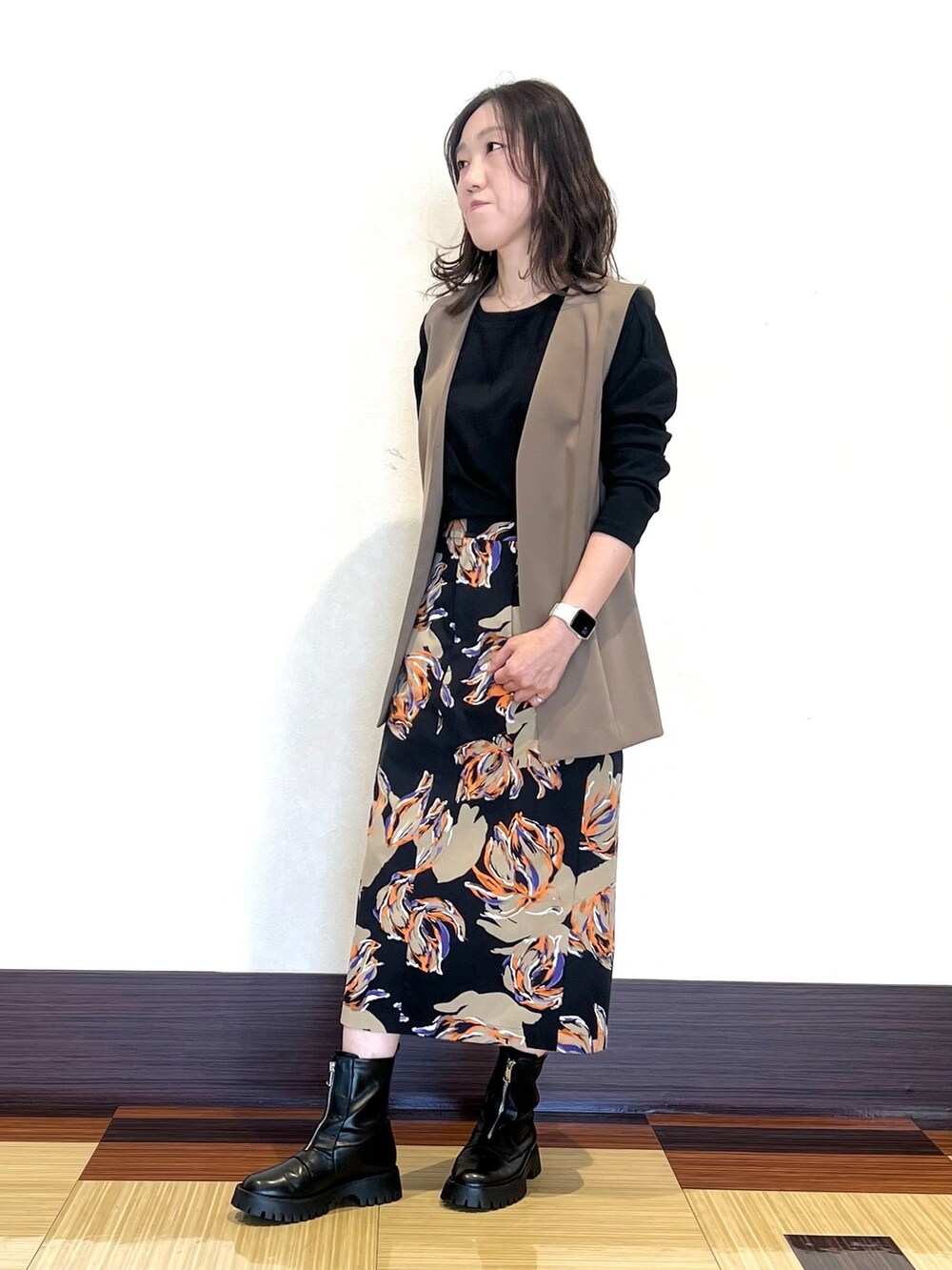 グレー系のTシャツ/カットソー、ブラウン系のベスト、ブラック系のスカートを着用したレディースの秋コーディネートの2枚目の写真