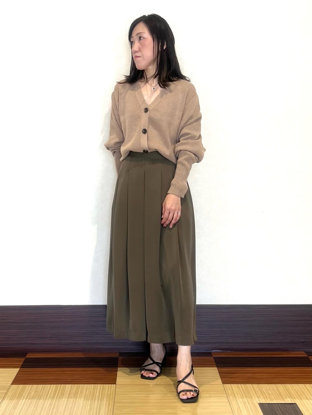 ベージュ系のカーディガン/ボレロ、グリーン系のスカート、ブラック系のサンダルを着用したレディースの秋コーディネートの4枚目の写真