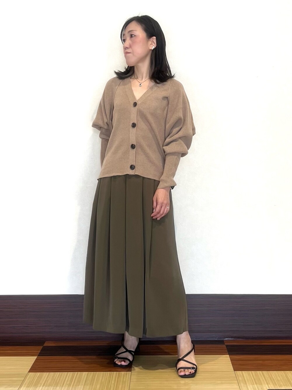 ベージュ系のカーディガン/ボレロ、グリーン系のスカート、ブラック系のサンダルを着用したレディースの秋コーディネートの3枚目の写真