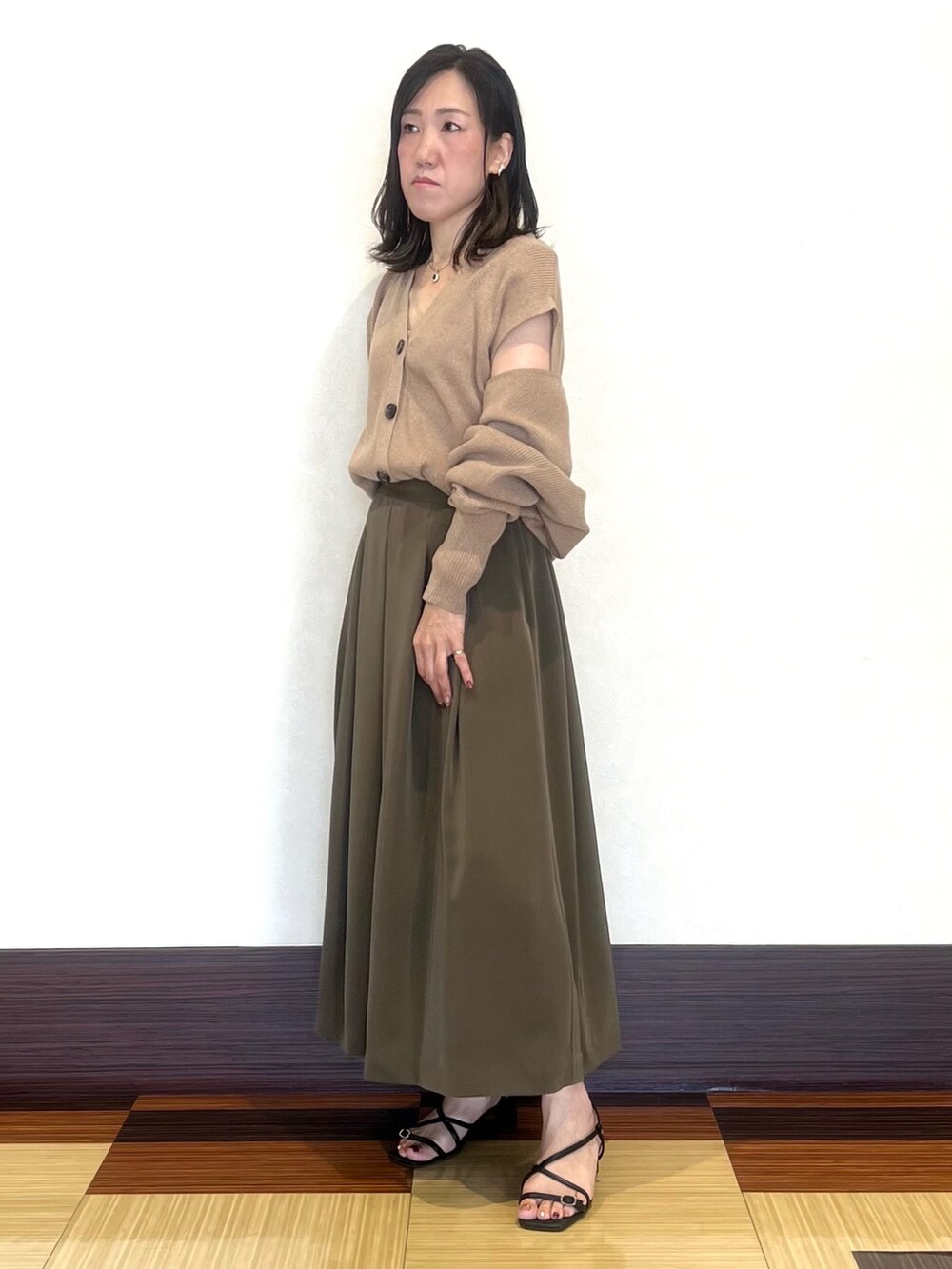ベージュ系のカーディガン/ボレロ、グリーン系のスカート、ブラック系のサンダルを着用したレディースの秋コーディネートの5枚目の写真