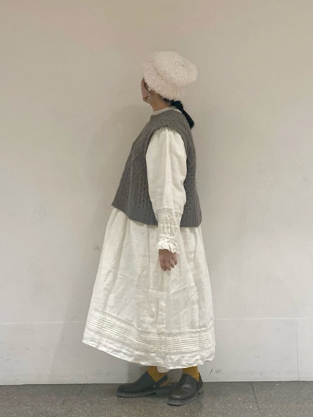 ブラウン系のベスト、ホワイト系のワンピース、ホワイト系のイヤリングを着用したレディースの冬コーディネートの2枚目の写真