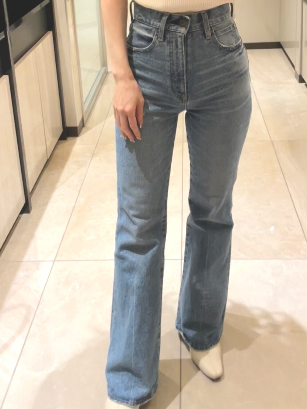 ブルー系のデニムパンツ、ホワイト系のショルダーバッグ、ホワイト系のニット/セーターを着用したレディースの春コーディネートの2枚目の写真