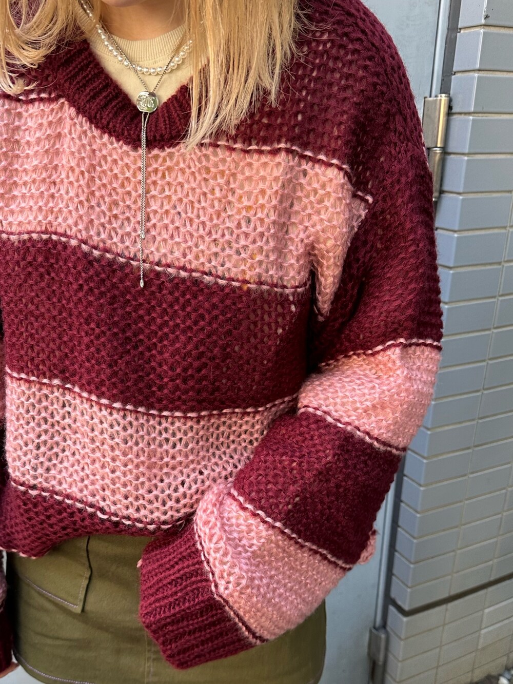 レッド系のニット/セーター、ホワイト系のTシャツ/カットソー、グリーン系のスカートを着用したレディースの秋コーディネートの4枚目の写真