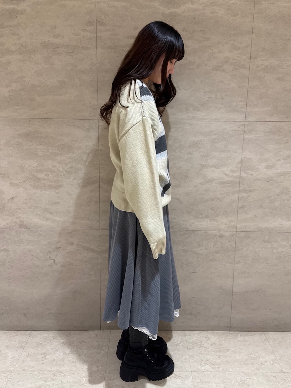 グレー系のスカート、ホワイト系のニット/セーター、ブラック系のブーツを着用したレディースの冬コーディネートの3枚目の写真