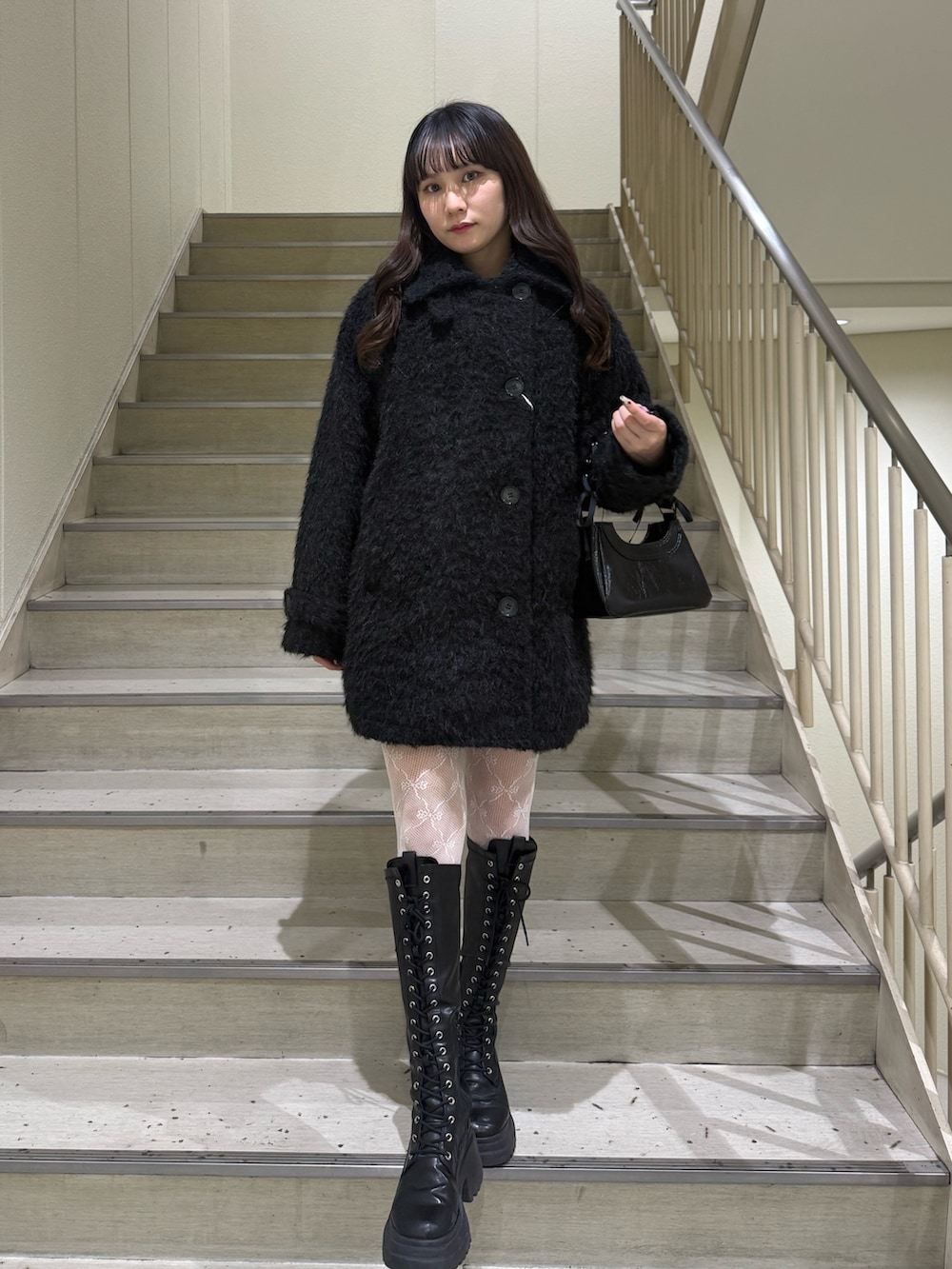 ブラック系のステンカラーコート、ブラック系のハンドバッグ、ブラック系のブーツを着用したレディースの冬コーディネートの2枚目の写真