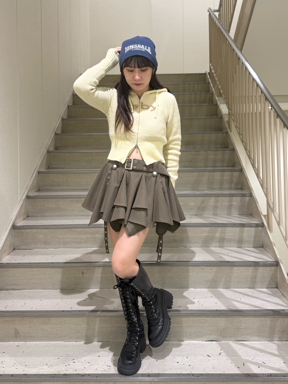 イエロー系のパーカー、ベージュ系のスカート、ブラック系のブーツを着用したレディースの冬コーディネートの5枚目の写真