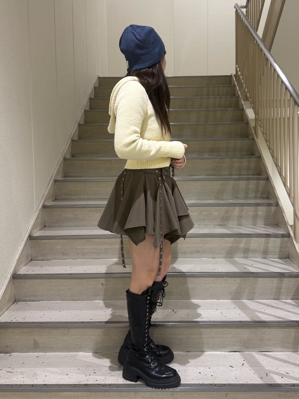 イエロー系のパーカー、ベージュ系のスカート、ブラック系のブーツを着用したレディースの冬コーディネートの4枚目の写真