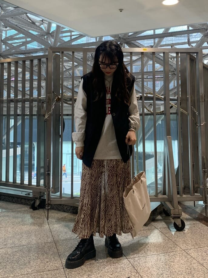 ブラック系のベスト、ホワイト系のトートバッグ、その他のスカートを着用したレディースの春コーディネートの2枚目の写真