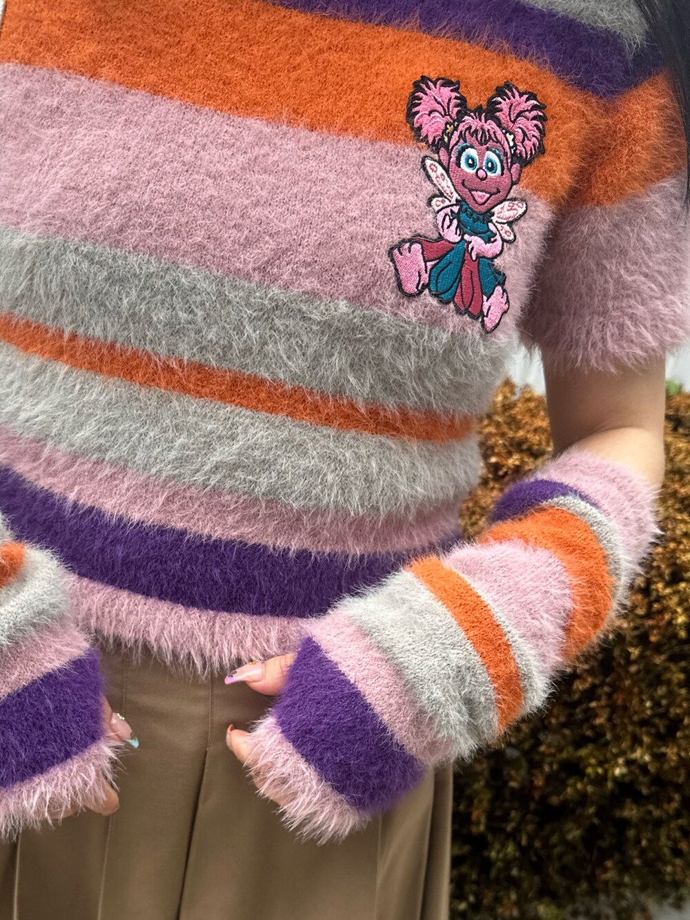 ピンク系のニット/セーター、ベージュ系のスカート、ホワイト系のショルダーバッグを着用したレディースの夏コーディネートの7枚目の写真