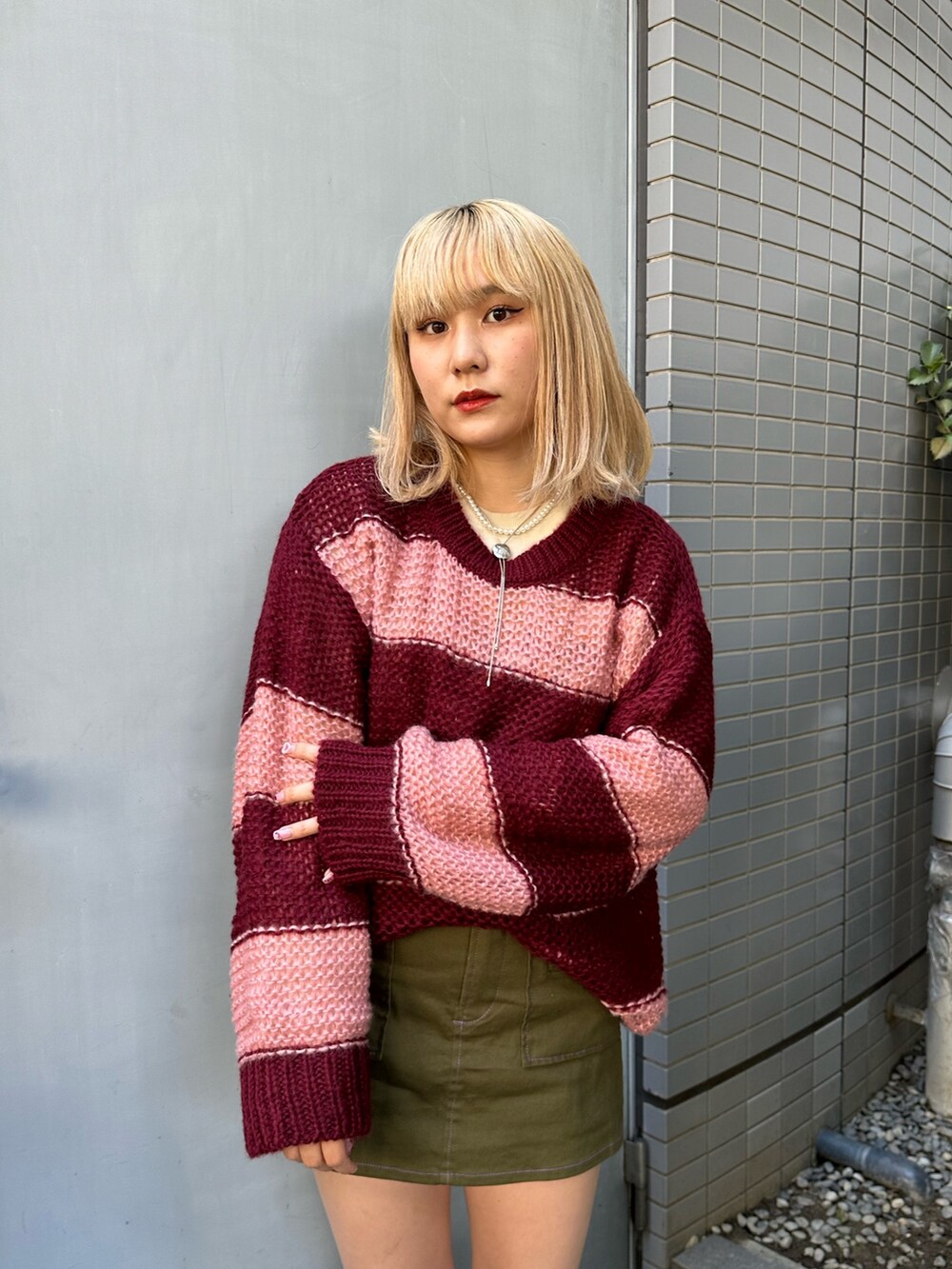 レッド系のニット/セーター、ホワイト系のTシャツ/カットソー、グリーン系のスカートを着用したレディースの秋コーディネートの3枚目の写真