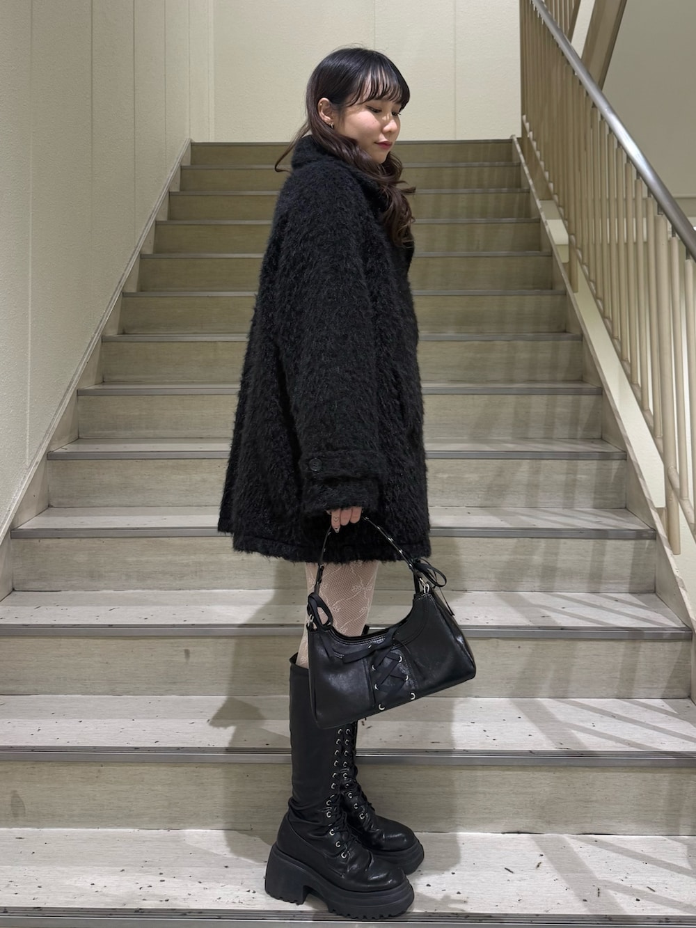 ブラック系のステンカラーコート、ブラック系のハンドバッグ、ブラック系のブーツを着用したレディースの冬コーディネートの4枚目の写真
