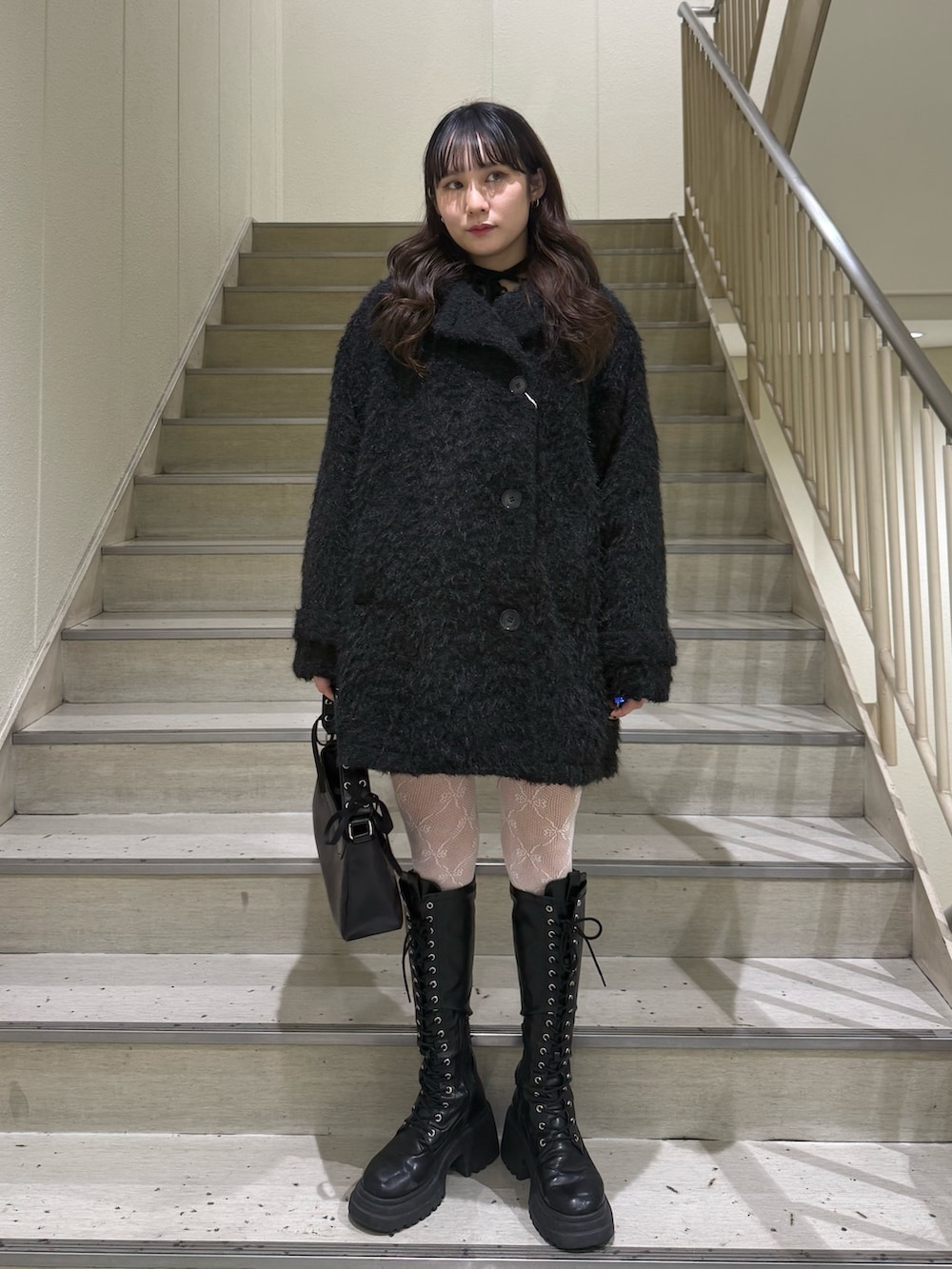 ブラック系のステンカラーコート、ブラック系のハンドバッグ、ブラック系のブーツを着用したレディースの冬コーディネートの5枚目の写真