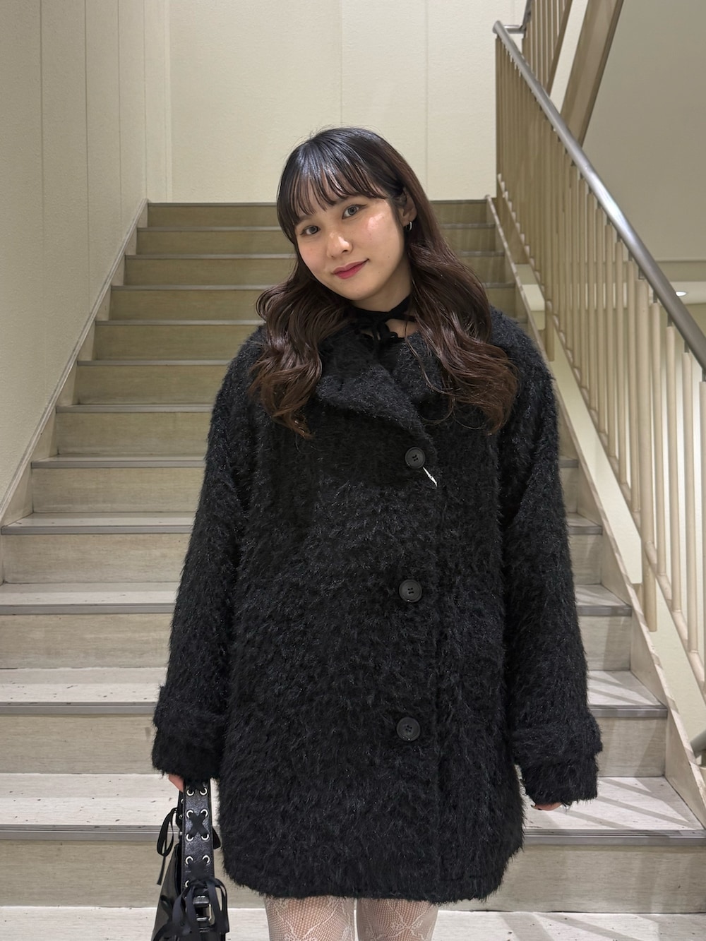 ブラック系のステンカラーコート、ブラック系のハンドバッグ、ブラック系のブーツを着用したレディースの冬コーディネートの6枚目の写真