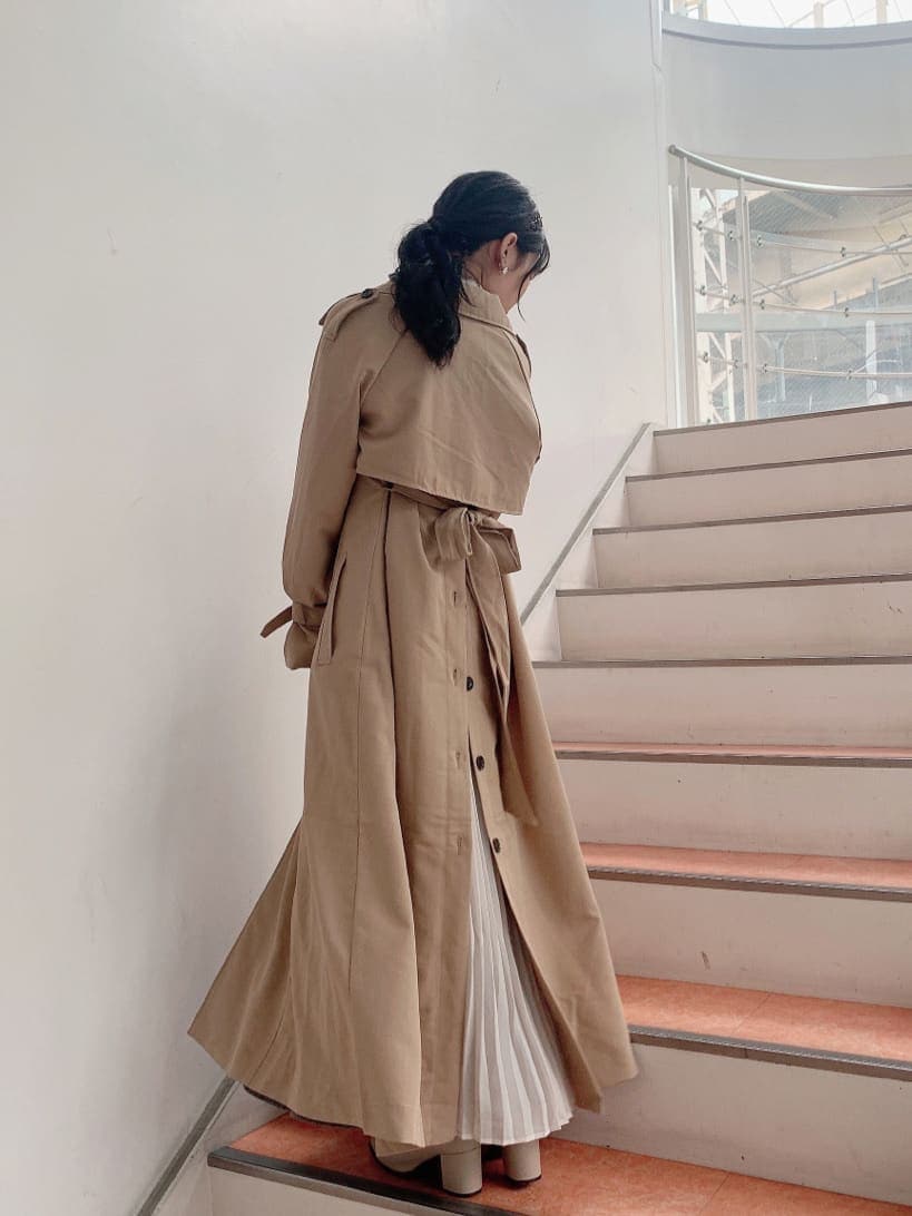 ベージュ系のトレンチコート、ベージュ系のブーツ、その他のジャンパースカートを着用したレディースの秋コーディネートの3枚目の写真