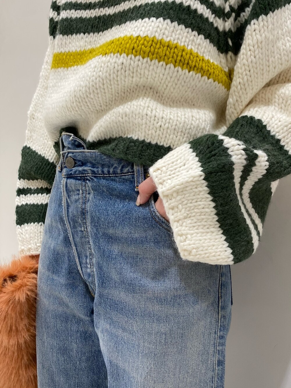 ブラック系のブーツ、オレンジ系のハンドバッグ、ブルー系のデニムパンツを着用したレディースの秋コーディネートの3枚目の写真