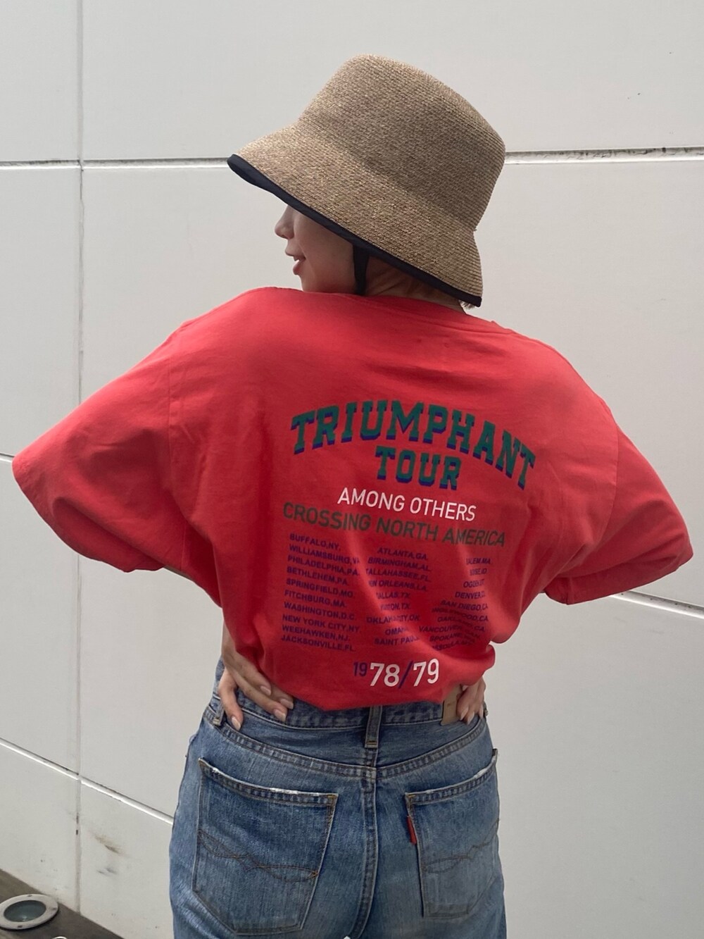 オレンジ系のTシャツ/カットソー、ホワイト系のスニーカー、ベージュ系のハットを着用したレディースの春コーディネートの2枚目の写真