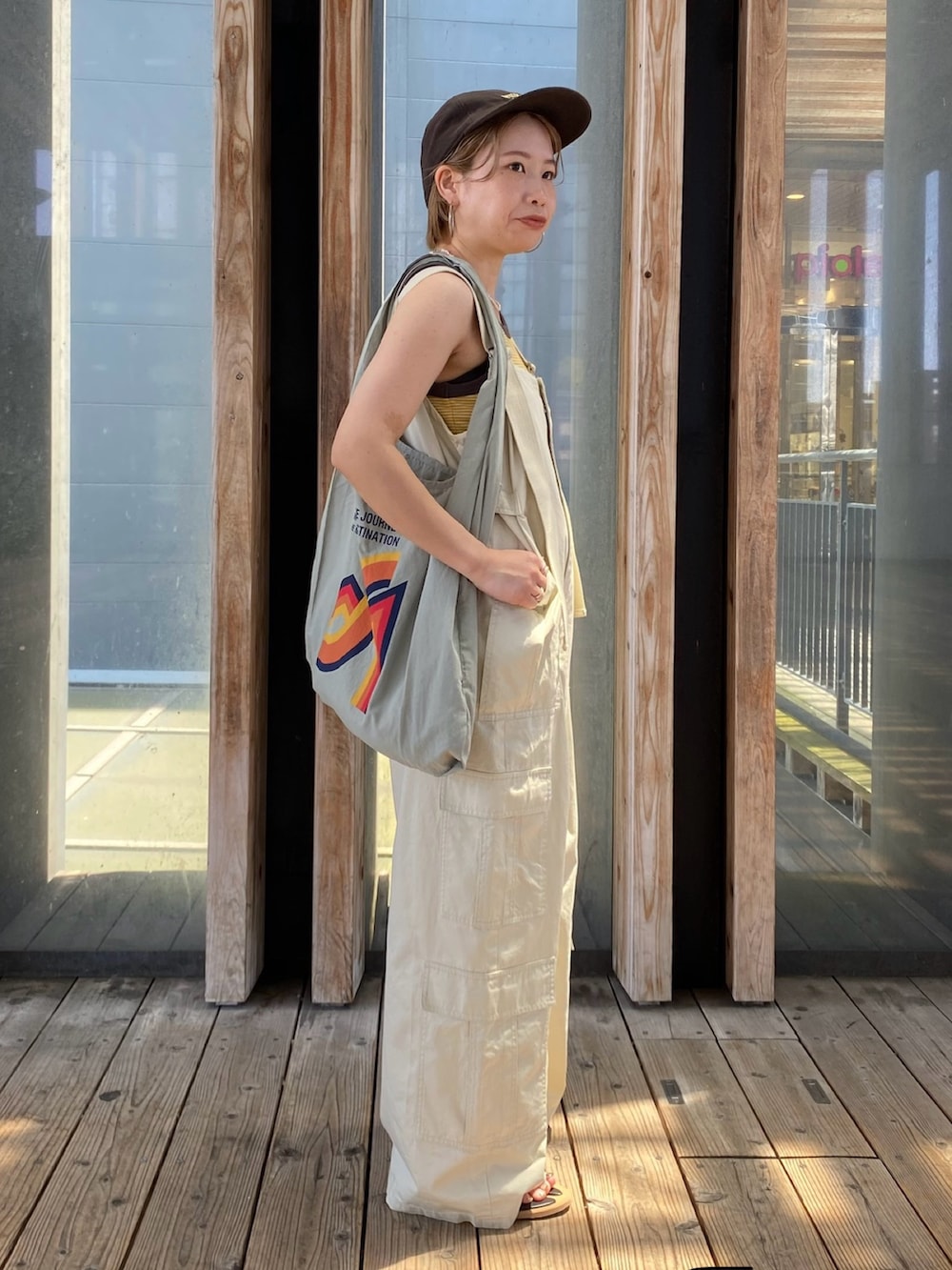 グリーン系のエコバッグ/サブバッグ、イエロー系のタンクトップ、ベージュ系のサロペット/オーバーオールを着用したレディースの夏コーディネートの2枚目の写真
