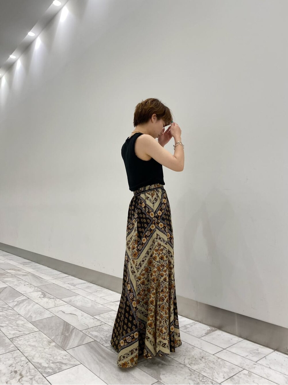 イエロー系のスカート、ブラック系のサンダル、ブラック系のタンクトップを着用したレディースの夏コーディネートの5枚目の写真