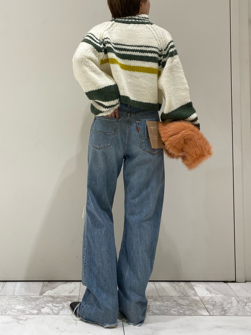 ブラック系のブーツ、オレンジ系のハンドバッグ、ブルー系のデニムパンツを着用したレディースの秋コーディネートの2枚目の写真