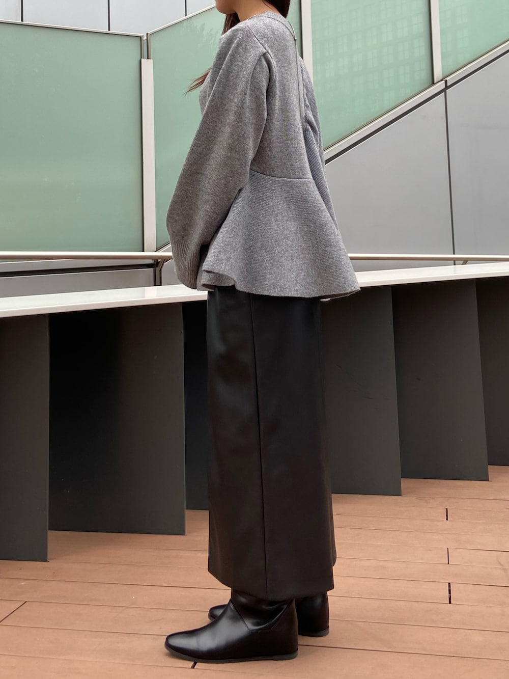 グレー系のニット/セーター、ブラック系のスカート、ブラック系のブーツを着用したレディースの秋コーディネートの2枚目の写真