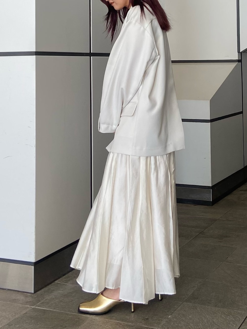ホワイト系のテーラードジャケット、ホワイト系のスカート、ゴールド系のサンダルを着用したレディースの冬コーディネートの2枚目の写真