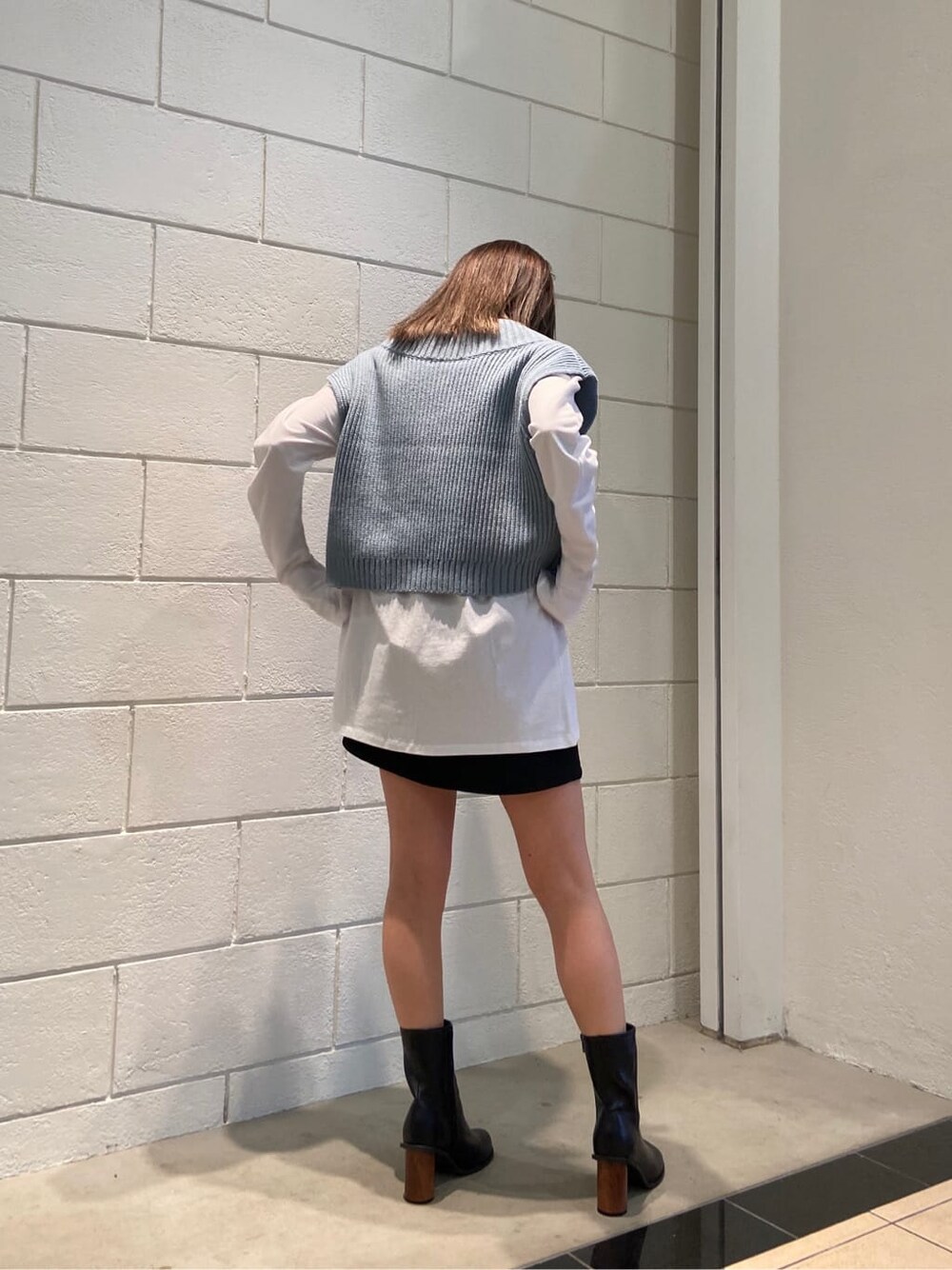 ブラック系のスカート、ブラック系のブーツ、ブルー系のベストを着用したレディースの春コーディネートの2枚目の写真