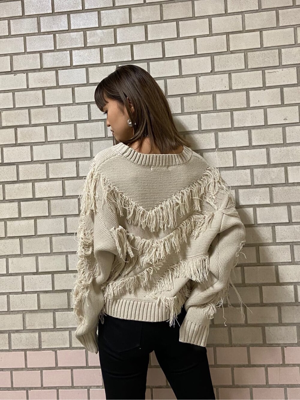 ブラック系のデニムパンツ、ホワイト系のハンドバッグ、ブラック系のブーツを着用したレディースの冬コーディネートの3枚目の写真