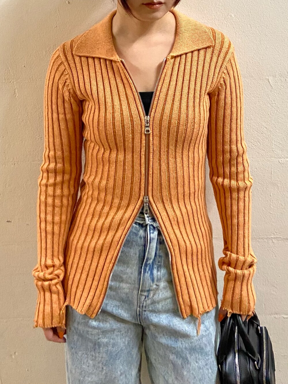 オレンジ系のニット/セーター、ブラック系のキャミソール、ブルー系のデニムパンツを着用したレディースの春コーディネートの4枚目の写真