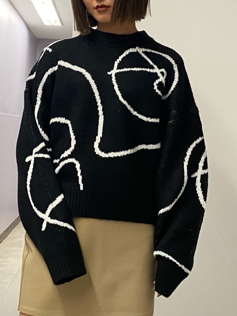 ブラック系のニット/セーター、ベージュ系のスカート、ブラック系のブーツを着用したレディースの秋コーディネートの5枚目の写真