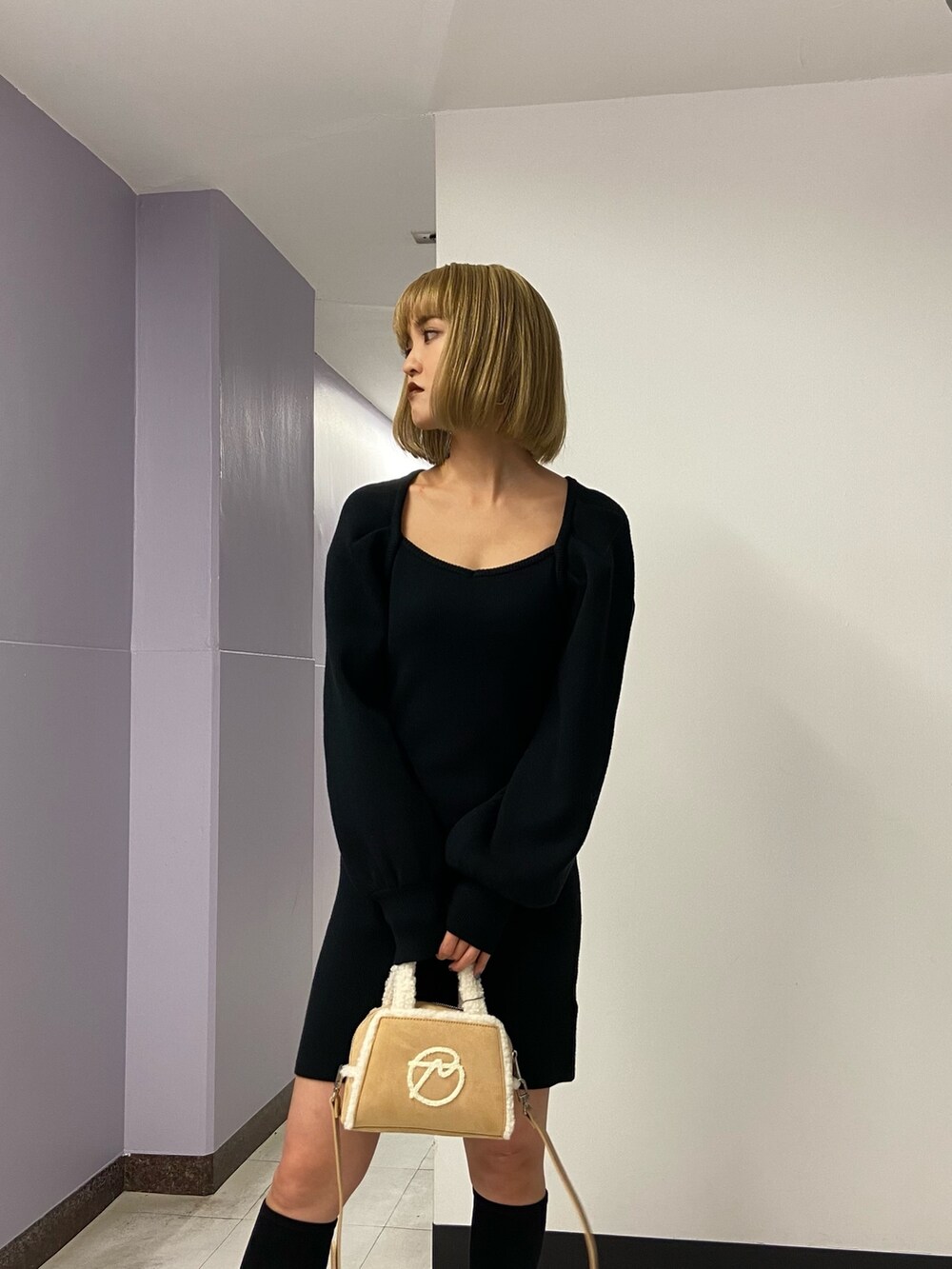 ブラック系のワンピース、ベージュ系のハンドバッグ、ブラック系のブーツを着用したレディースの冬コーディネートの6枚目の写真