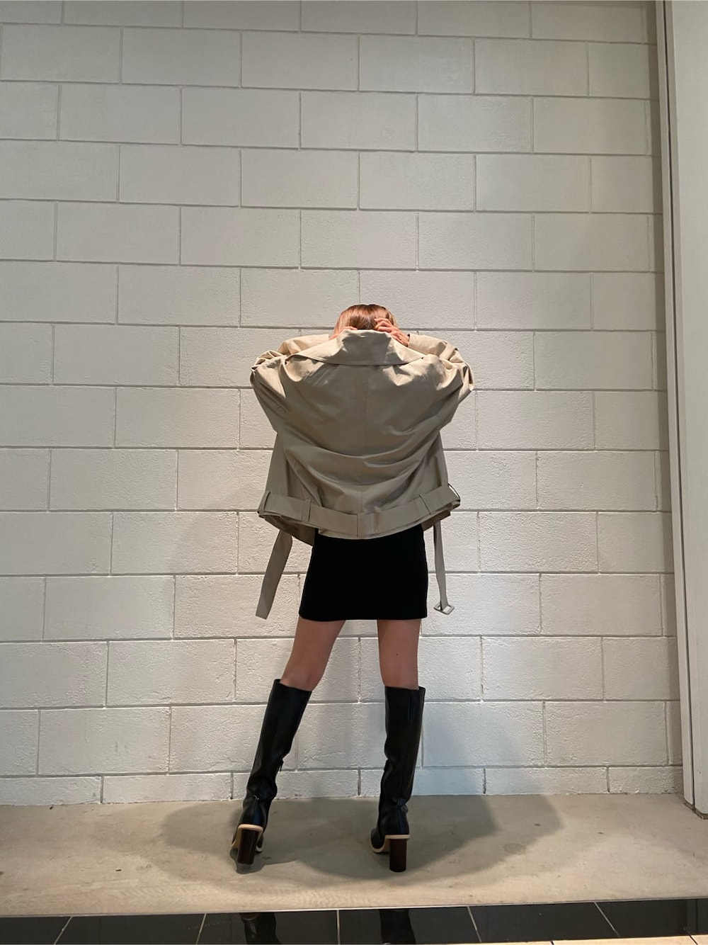 ブラック系のワンピース、ベージュ系のトレンチコート、ブラック系のブーツを着用したレディースの冬コーディネートの2枚目の写真