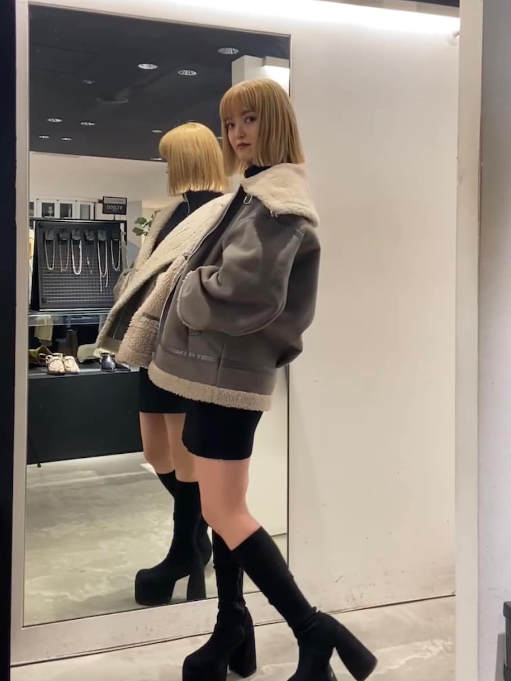 グレー系のブルゾン、ブラック系のワンピース、ブラック系のブーツを着用したレディースの冬コーディネートの2枚目の写真