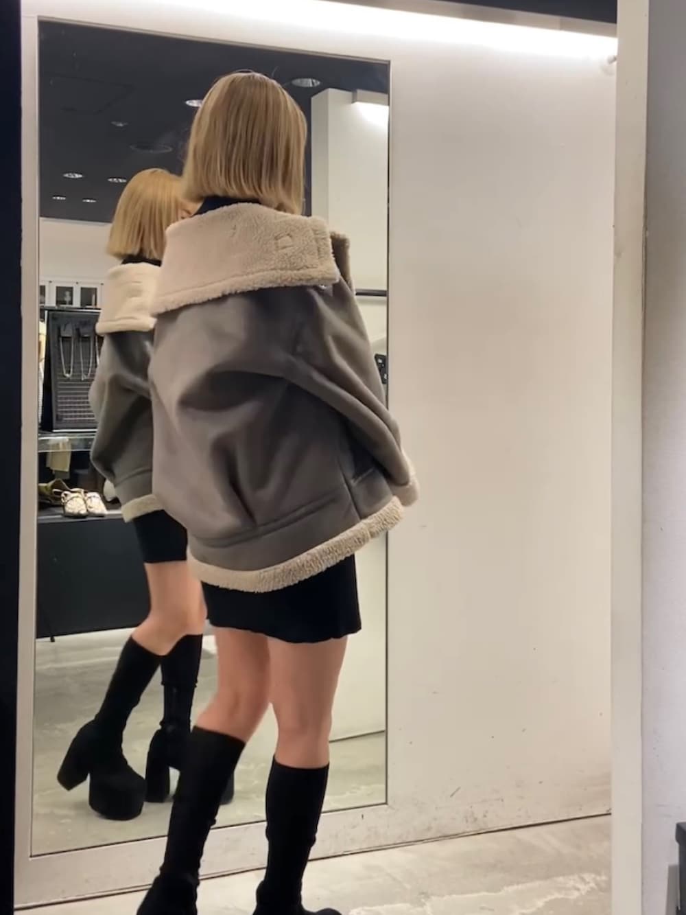 グレー系のブルゾン、ブラック系のワンピース、ブラック系のブーツを着用したレディースの冬コーディネートの3枚目の写真