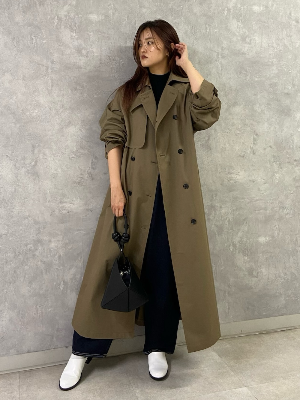 ブラウン系のトレンチコート、ブラック系のニット/セーター、ブルー系のデニムパンツを着用したレディースの秋コーディネートの2枚目の写真