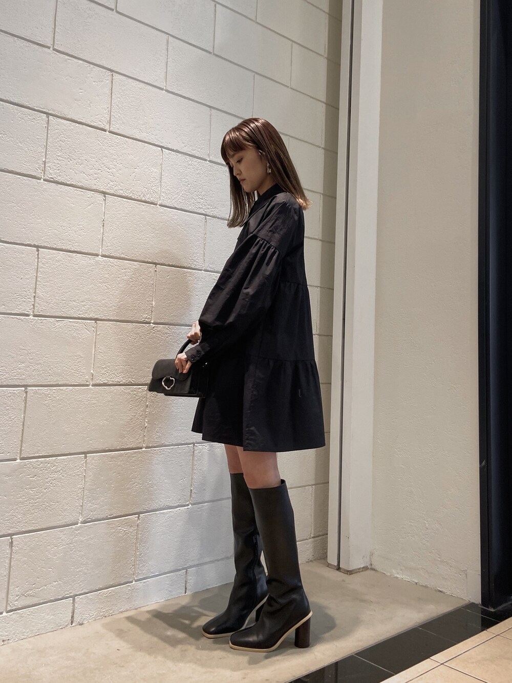 ブラック系のシャツワンピース、ブラック系のブーツ、ブラック系のハンドバッグを着用したレディースの冬コーディネートの2枚目の写真