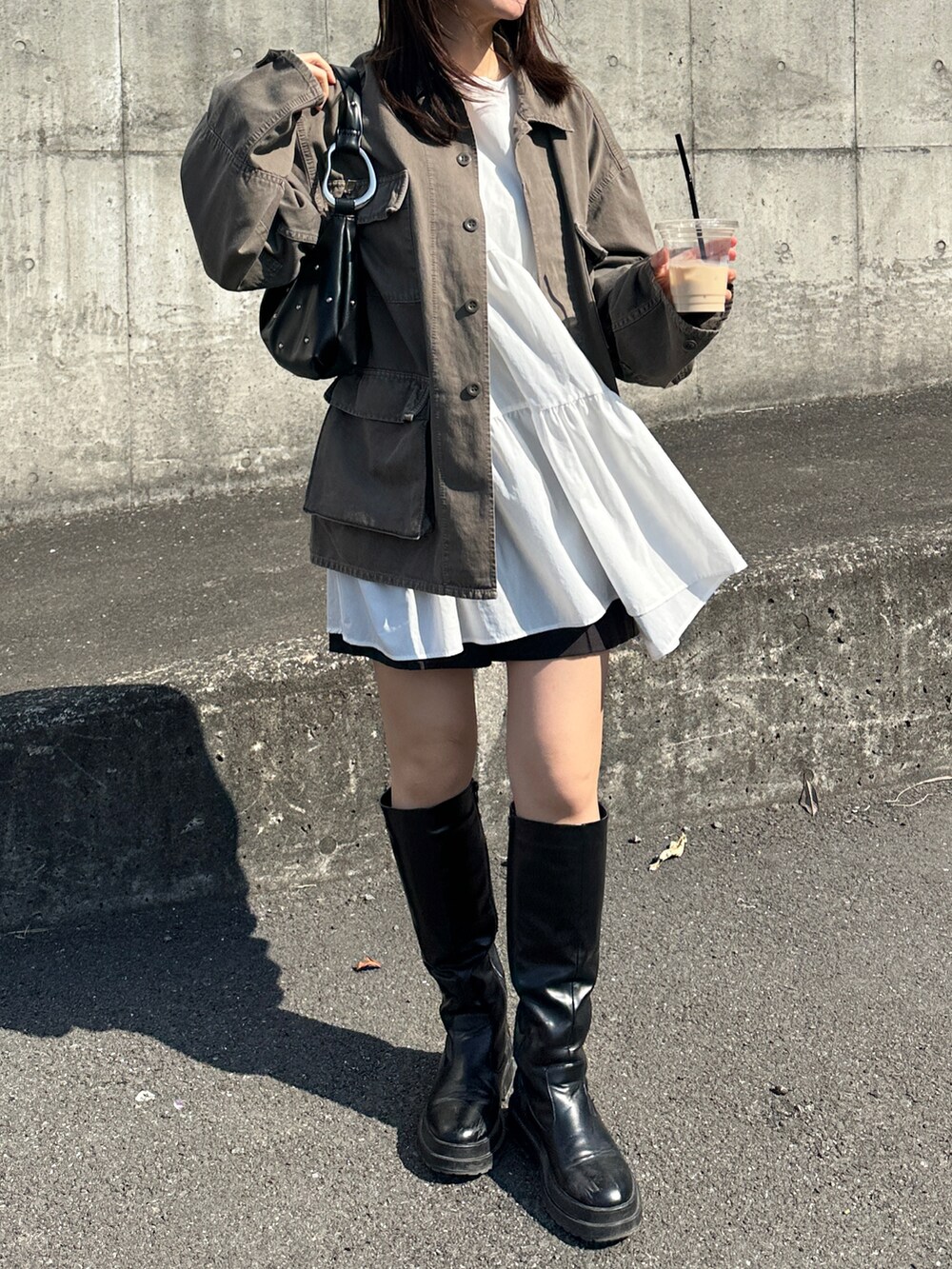 ブラウン系のデニムジャケット、ブラック系のハンドバッグ、ブラック系のブーツを着用したレディースの春コーディネートの2枚目の写真