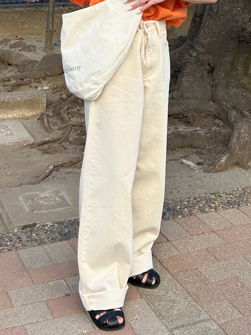 オレンジ系のTシャツ/カットソー、ホワイト系のハンドバッグ、ホワイト系のデニムパンツを着用したレディースの春コーディネートの7枚目の写真