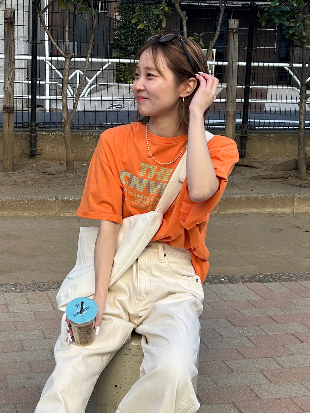 オレンジ系のTシャツ/カットソー、ホワイト系のハンドバッグ、ホワイト系のデニムパンツを着用したレディースの春コーディネートの5枚目の写真