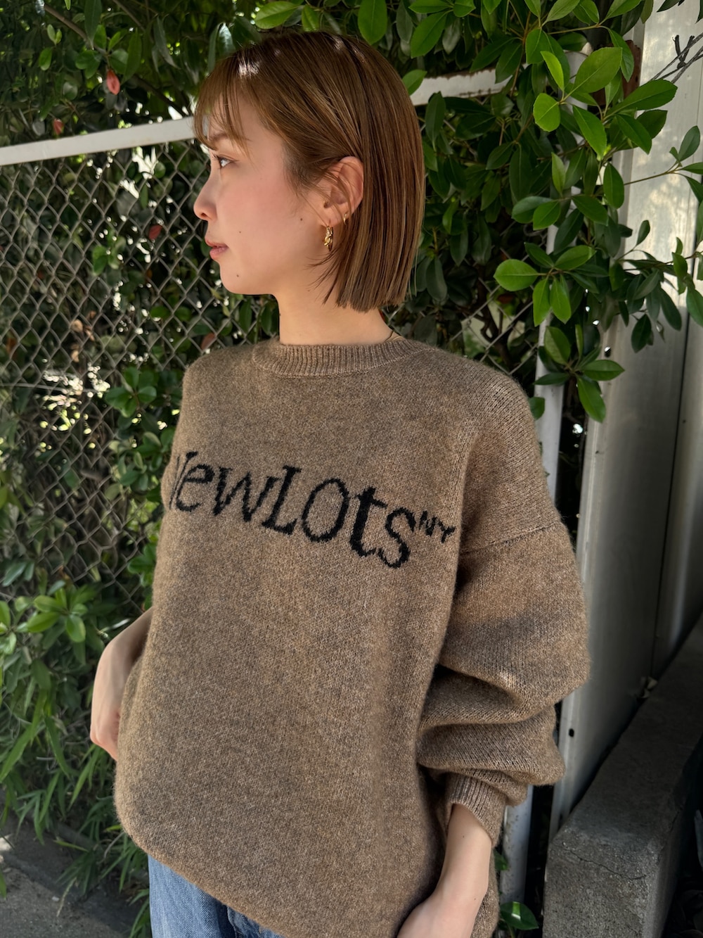 ブラック系のスニーカー、ベージュ系のニット/セーター、ブルー系のデニムパンツを着用したレディースの夏コーディネートの6枚目の写真