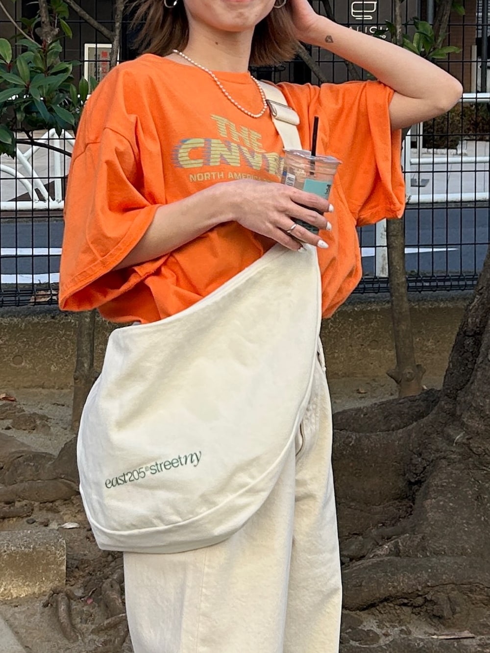 オレンジ系のTシャツ/カットソー、ホワイト系のハンドバッグ、ホワイト系のデニムパンツを着用したレディースの春コーディネートの6枚目の写真