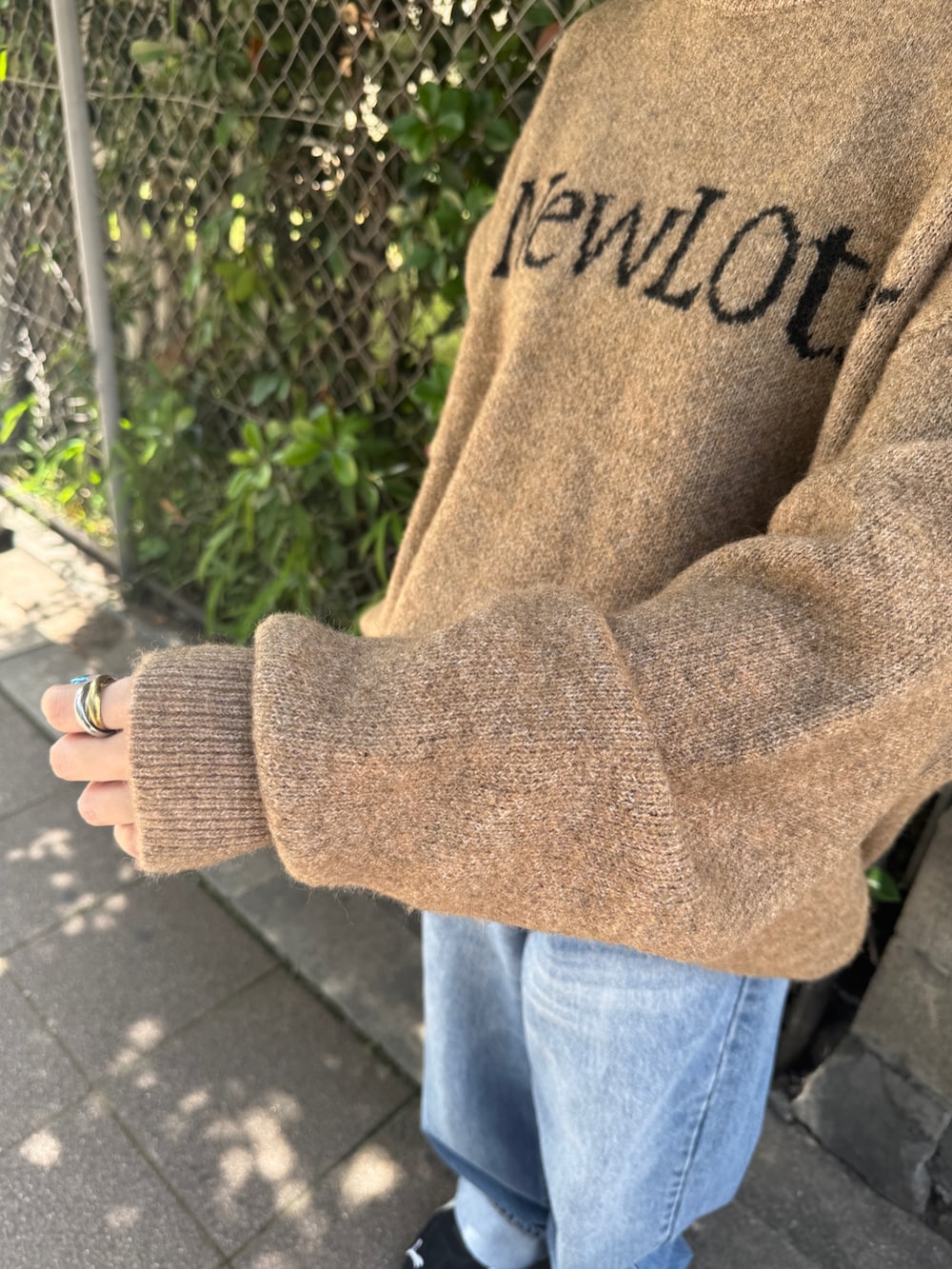 ブラック系のスニーカー、ベージュ系のニット/セーター、ブルー系のデニムパンツを着用したレディースの夏コーディネートの7枚目の写真