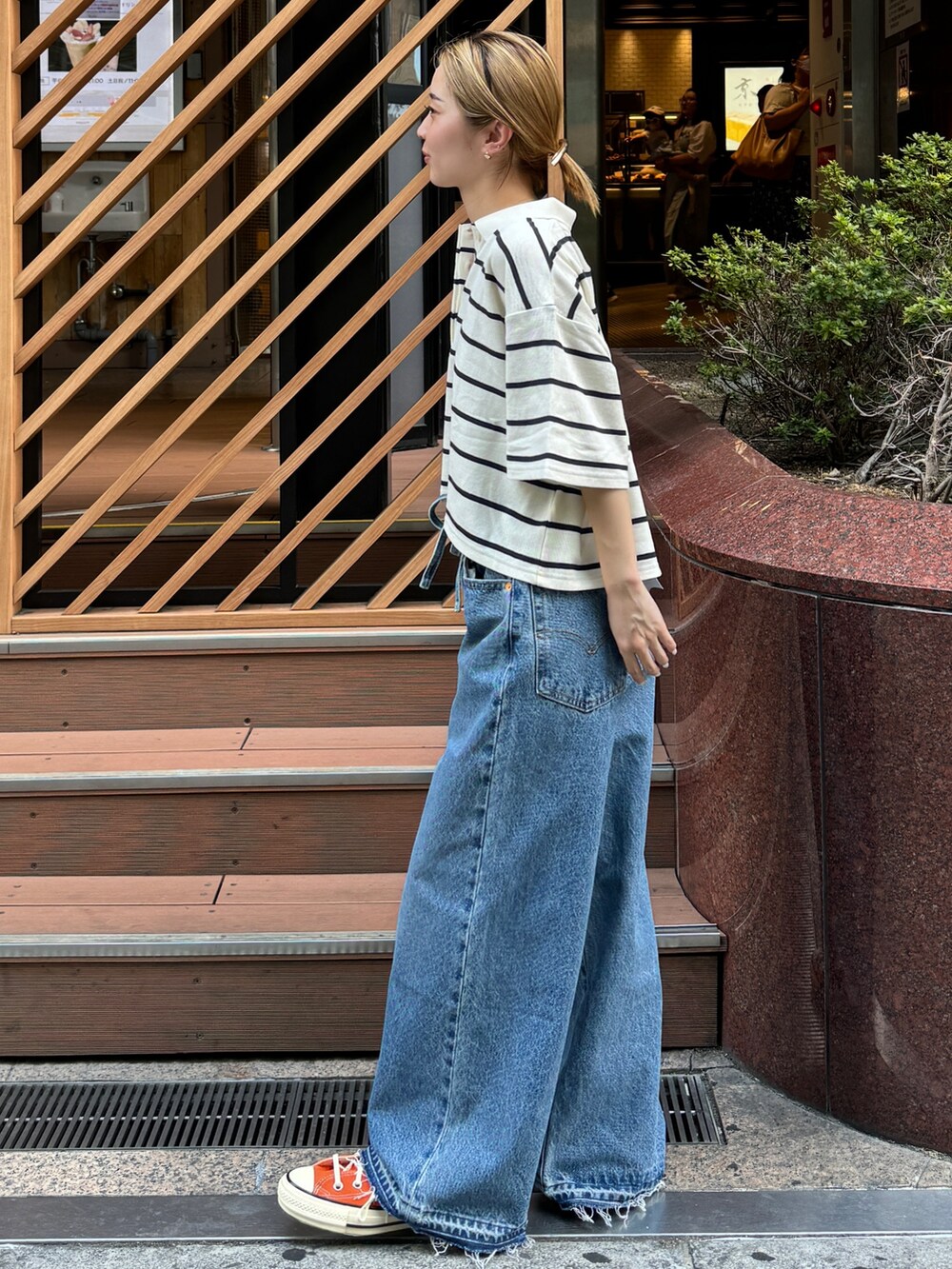 ホワイト系のポロシャツ、オレンジ系のスニーカー、ブルー系のデニムパンツを着用したレディースの夏コーディネートの2枚目の写真