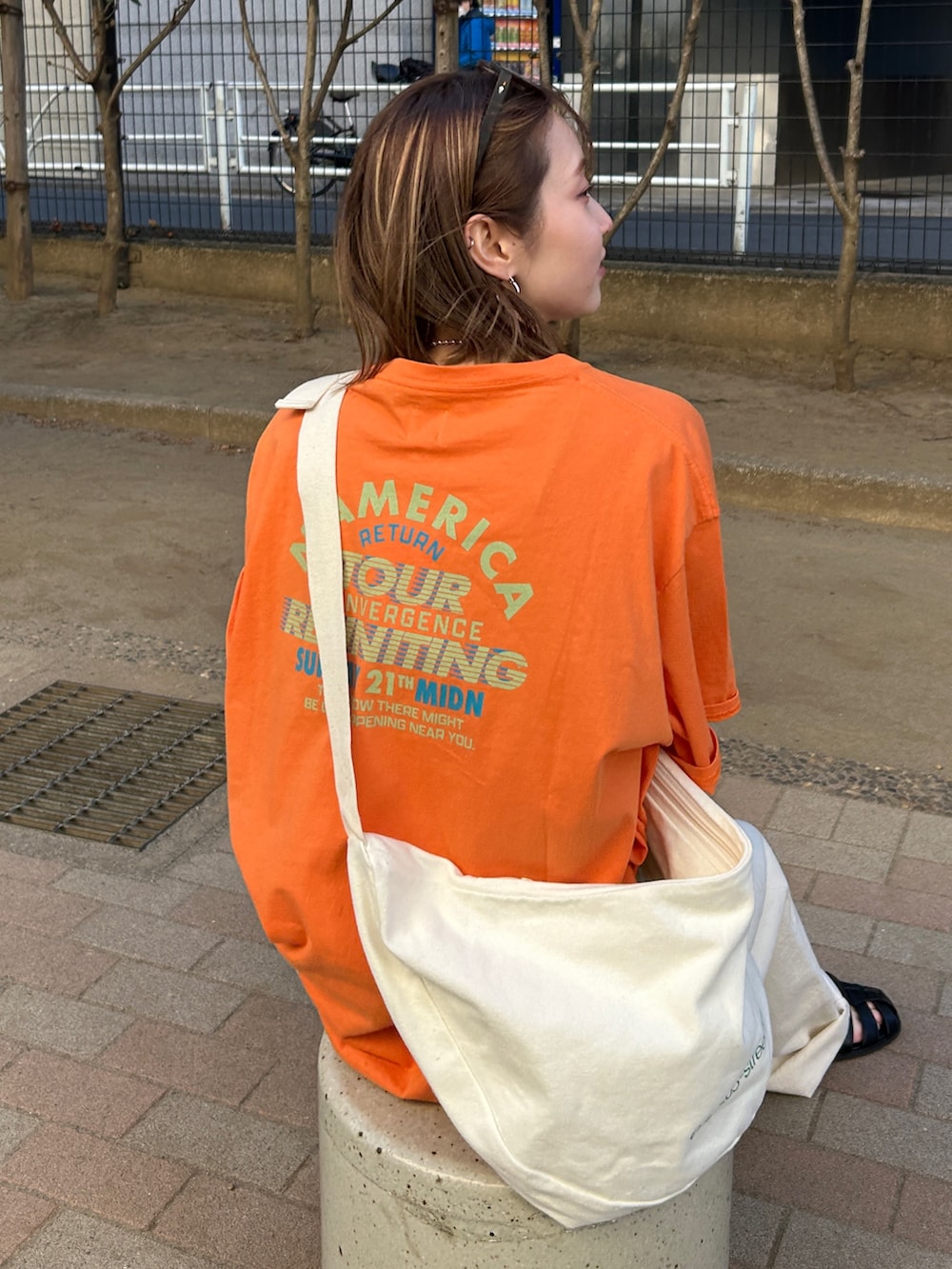 オレンジ系のTシャツ/カットソー、ホワイト系のハンドバッグ、ホワイト系のデニムパンツを着用したレディースの春コーディネートの3枚目の写真