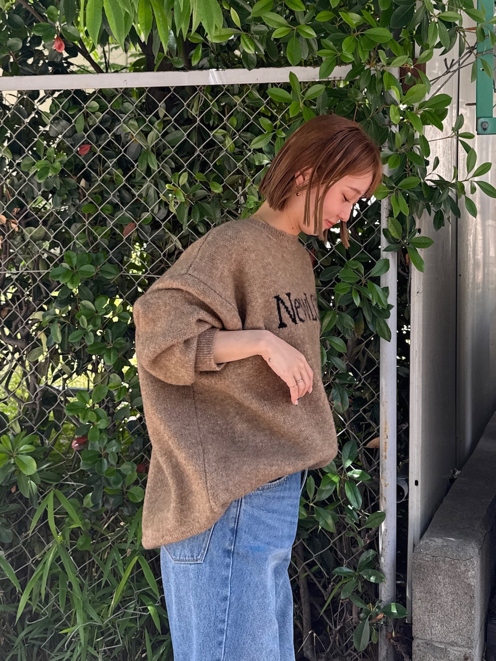 ブラック系のスニーカー、ベージュ系のニット/セーター、ブルー系のデニムパンツを着用したレディースの夏コーディネートの5枚目の写真