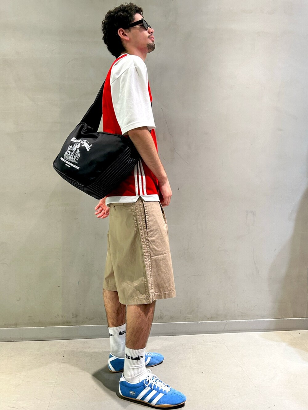 レッド系のタンクトップ、ブルー系のスニーカー、ブラック系のショルダーバッグを着用したメンズの春コーディネートの2枚目の写真