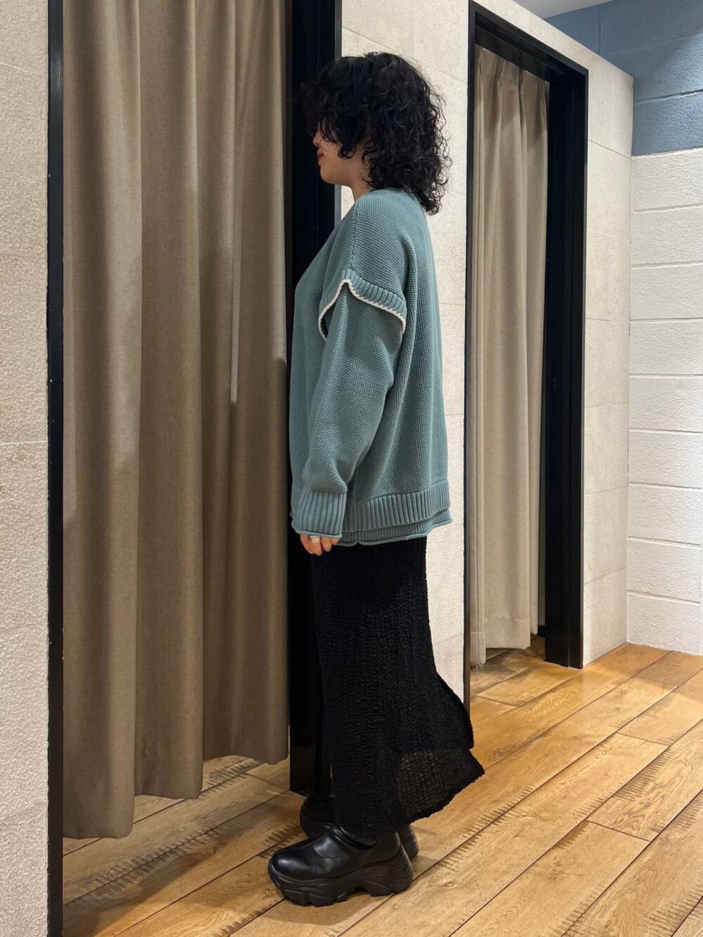 グリーン系のニット/セーター、ブラック系のブーツ、ブラック系のスカートを着用したレディースの秋コーディネートの2枚目の写真