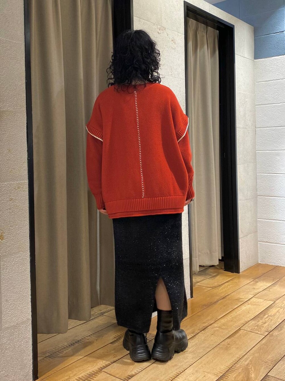 レッド系のニット/セーター、ブラック系のブーツ、ブラック系のスカートを着用したレディースの冬コーディネートの3枚目の写真