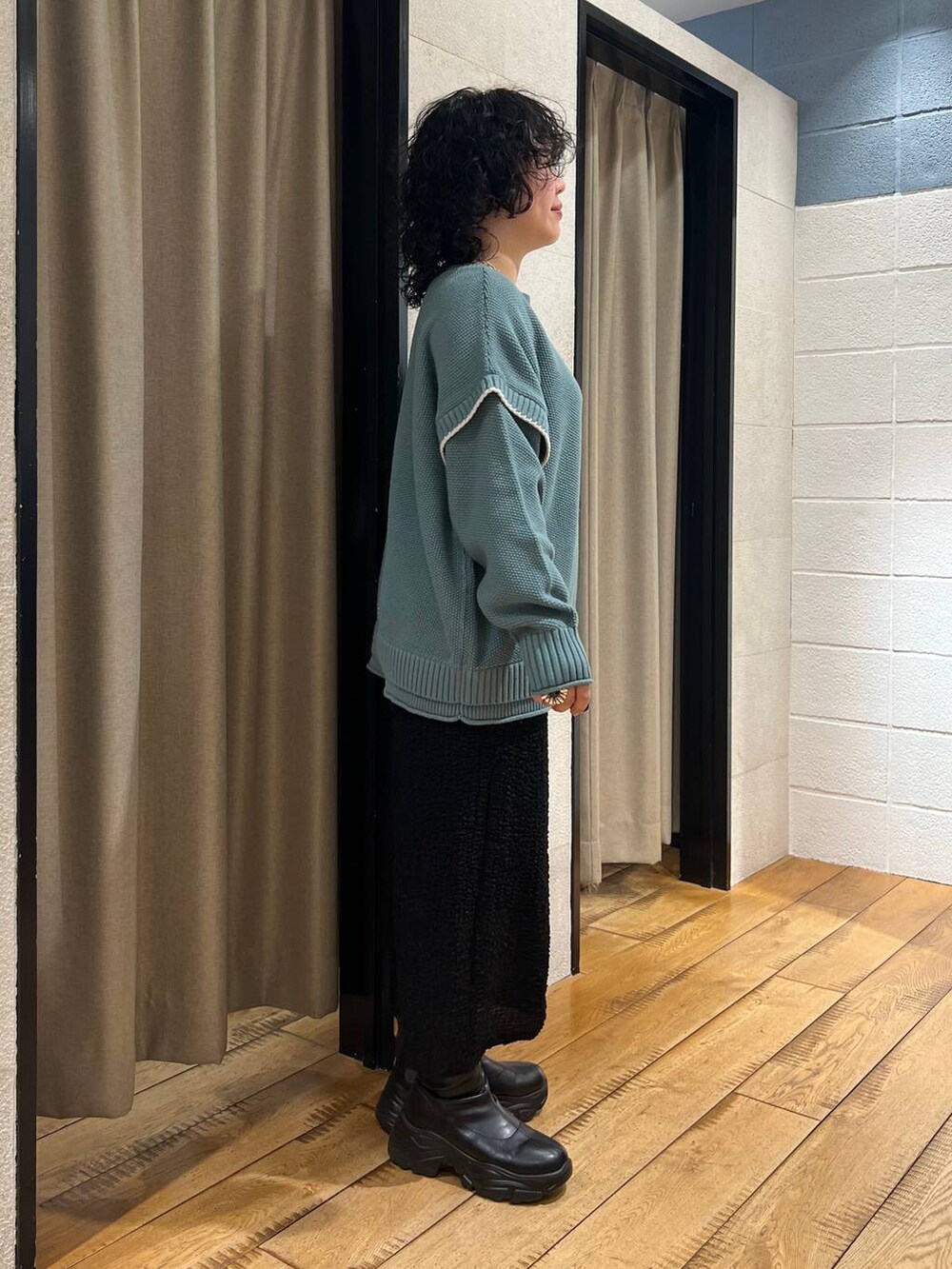 グリーン系のニット/セーター、ブラック系のブーツ、ブラック系のスカートを着用したレディースの秋コーディネートの4枚目の写真